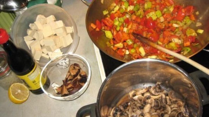 Eine Tofupfanne mit Gem&uuml;se wird zubereitet, w&auml;hrend angebratene Pilze in einem Topf k&ouml;cheln und frisches Gem&uuml;se in einer Pfanne br&auml;t.