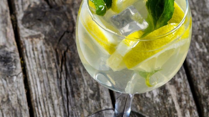 Ein Glas mit einem erfrischenden alkoholfreien Sommergetr&auml;nk, gef&uuml;llt mit Eis, Zitronenscheiben und Minze, steht auf einem Holztisch.