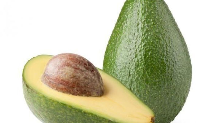 Eine ganze und eine halbierte gr&uuml;ne Avocado liegen nebeneinander auf einem wei&szlig;en Hintergrund.