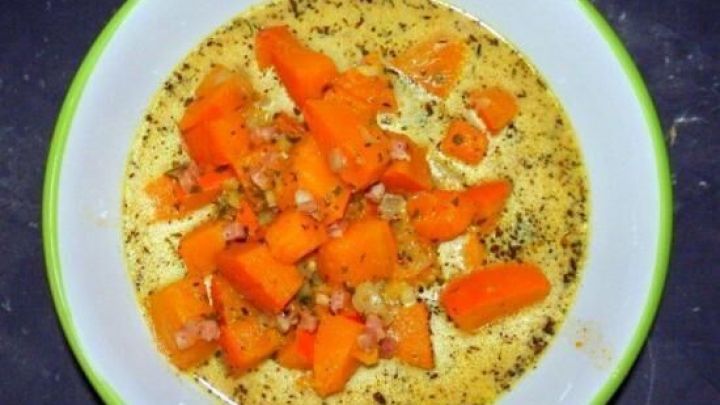 Eine cremige K&uuml;rbissuppe mit st&uuml;ckigen K&uuml;rbisw&uuml;rfeln, serviert in einer wei&szlig;en Sch&uuml;ssel auf einem dunklen Tisch.