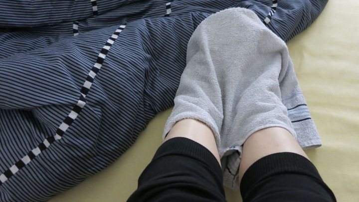 F&uuml;&szlig;e, eingewickelt in ein feuchtes Handtuch, liegen in einem Bett mit blau-gestreifter Bettw&auml;sche, um die Hitze zu lindern.