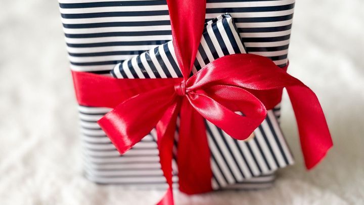 Ein sorgf&auml;ltig verpacktes Geschenk in Streifenpapier mit rotem Band liegt auf einem flauschigen Untergrund und zieht Aufmerksamkeit auf sich.