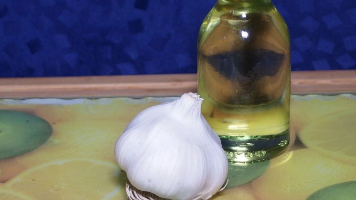 Eine Knoblauchzehe liegt neben einer Flasche &Ouml;l auf einem bunten Tisch. Sie symbolisieren die Zubereitung von Knoblauch&ouml;l.