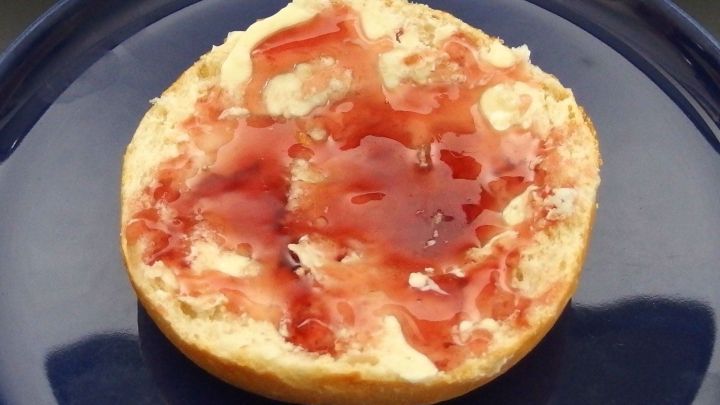 Ein Br&ouml;tchen mit rotem Holunder Gelee liegt auf einem blauen Teller und sorgt f&uuml;r ein einladendes Fr&uuml;hst&uuml;cksgef&uuml;hl.