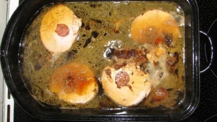 Saftige K&uuml;mmelkoteletts kochen in einer Auflaufform, umgeben von aromatischer Sauce auf einem Herd.