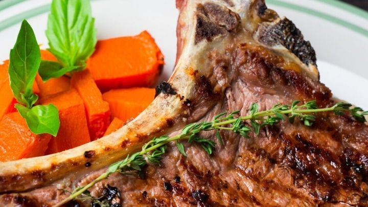 Koteletts mit einer knusprigen Pilzhaube liegen auf einem Teller, umgeben von K&uuml;rbis und frischen Tomaten.