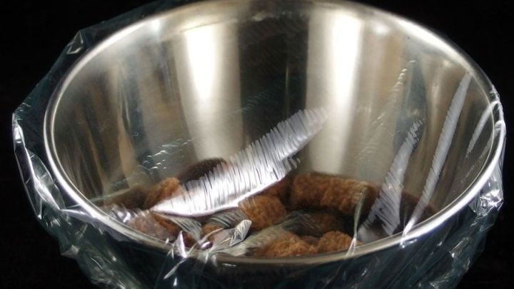 Eine Sch&uuml;ssel ist mit Frischhaltefolie abgedeckt, w&auml;hrend sie sich in einem dunklen Raum befindet, um den Inhalt frisch zu halten.