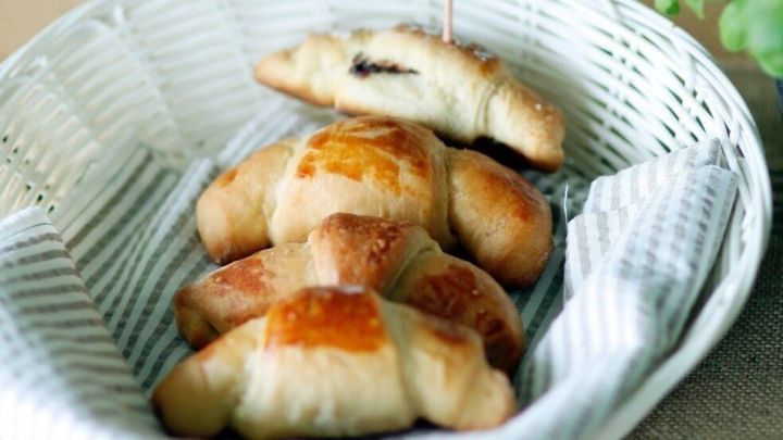 In einem Korb liegen goldbraune Fr&uuml;hst&uuml;cksh&ouml;rnchen, w&auml;hrend sie auf einem rustikalen Holztisch pr&auml;sentiert werden.