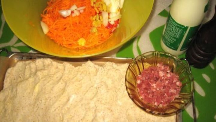 Ein vorbereiteter Teig f&uuml;r w&uuml;rzigen K&uuml;rbiskuchen liegt auf einem Blech, umgeben von geschnittenem Gem&uuml;se und Zutaten.