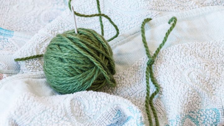 Ein gr&uuml;ner Wollkn&auml;uel liegt auf einem wei&szlig;en Handtuch, w&auml;hrend ein gr&uuml;nes St&uuml;ck Faden sichtbar danebenliegt.