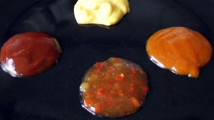 Auf einem schwarzen Teller liegen verschiedene So&szlig;enh&auml;ufchen: Ketchup, Chili, und eine gelbe So&szlig;e, ideal zum Chili.