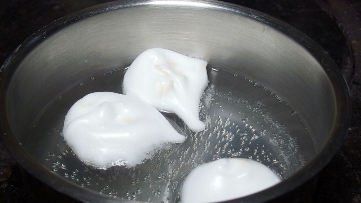 Drei schaumige Eiwei&szlig;kugeln schwimmen in einem Topf mit kochendem Wasser, bereit zum Garen f&uuml;r das Dessert.