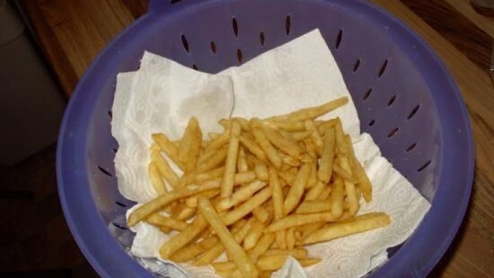 Pommes liegen in einem Sieb auf K&uuml;chenpapier, um nach dem Frittieren Fettreste abzutropfen.