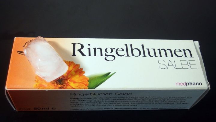 Eine Tube Ringelblumensalbe steht auf einem dunklen Hintergrund, bereit zur Linderung von Rasurirritationen und Intimpickelchen.