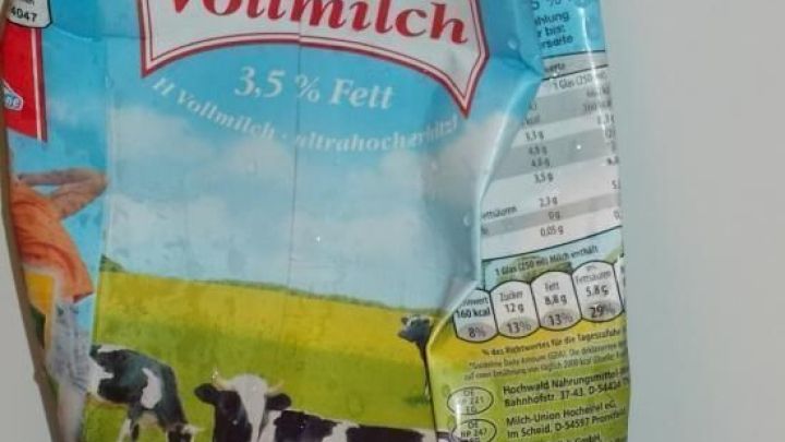 Eine Milchpackung steht auf einem Tisch, mit Bildern von K&uuml;hen und einer Wiese, die frische H-Milch zeigt.