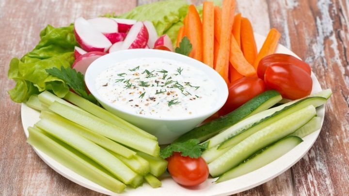 Ein Teller mit frischem Gem&uuml;se wie Karotten, Gurken und Tomaten wird mit einem Dip serviert, auf einem Holztisch platziert.