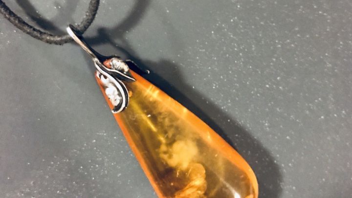 Ein eleganter Bernstein-Anh&auml;nger schwingt an einer Schnur, funkelnd und warm, auf einem neutralen Hintergrund.