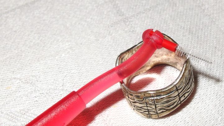 Ein Interdentalb&uuml;rste reinigt Silberschmuck, w&auml;hrend sie auf einem hellen Tuch liegt, um Schmutz zu entfernen.