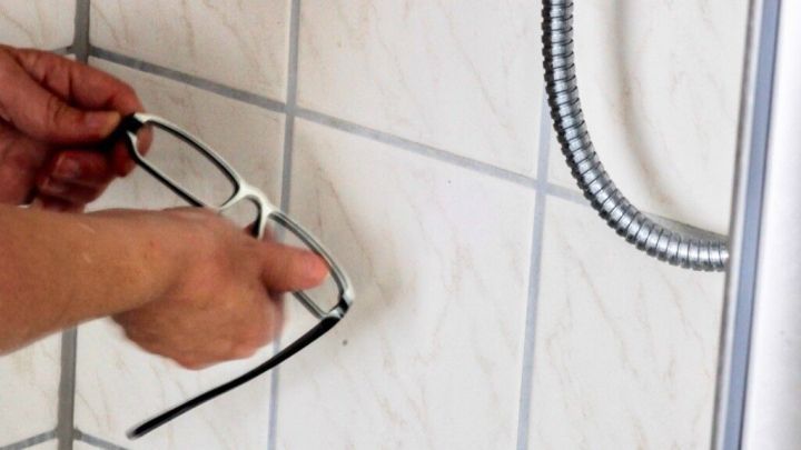 Eine Person h&auml;lt eine Brille und reinigt sie unter einem Duschkopf mit Haarshampoo, um sie zu s&auml;ubern.