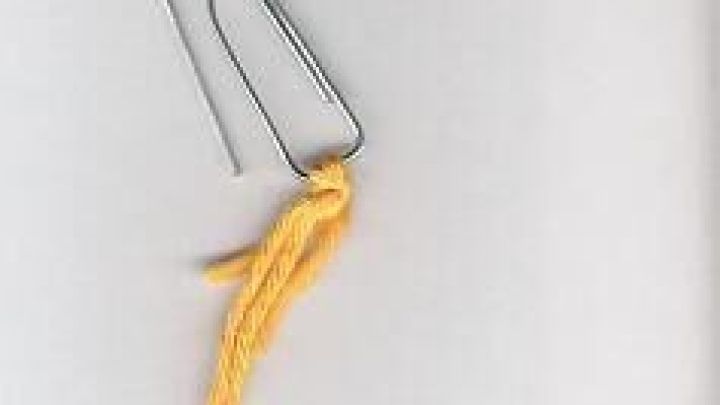 Ein silberner Rei&szlig;verschlussanheber aus Metall mit einem gelben Faden, der zum Schlie&szlig;en und &Ouml;ffnen von Rei&szlig;verschl&uuml;ssen dient.