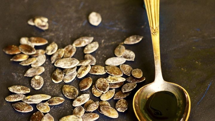 K&uuml;rbiskerne und ein L&ouml;ffel mit dunklem &Ouml;l liegen auf einem dunklen Hintergrund und deuten auf nat&uuml;rliche Produkte zur Prostatast&auml;rkung hin.