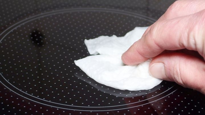 Ein Handtuch reinigt ein Glaskeramikfeld, w&auml;hrend es von einer Person nach einem &Uuml;berkochen schnell ges&auml;ubert wird.