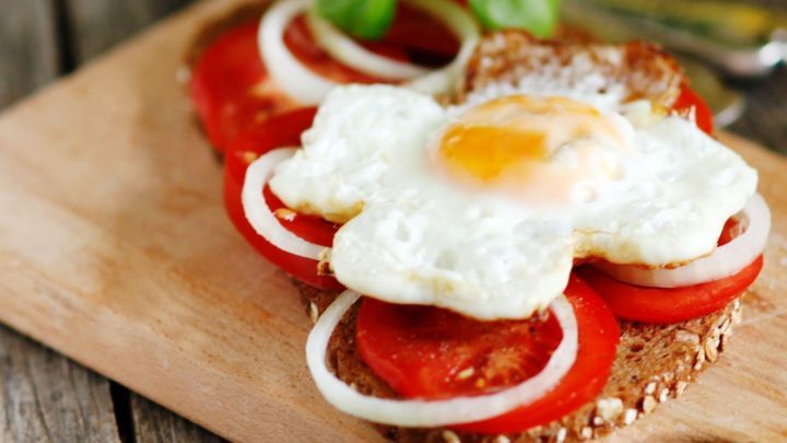 Ein belegtes Brot mit frischen Tomaten, Zwiebeln und einem Spiegelei, auf einem Holzbrett angerichtet.