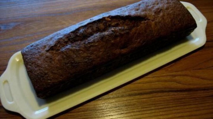 Ein Schoko-Aprikosen-Kuchen liegt auf einer wei&szlig;en Platte, umgeben von einem warmen Holzuntergrund.