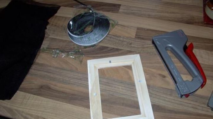 Ein Holzrahmen liegt auf einem Tisch, umgeben von Werkzeugen und einer Schnur, bereit zur Aufbewahrung von Ohrsteckern.