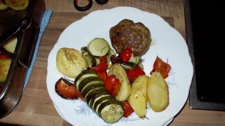 Eine Portion Frikadellen liegt auf einem Teller, umgeben von Ofengem&uuml;se wie Zucchini, Kartoffeln und Paprika.