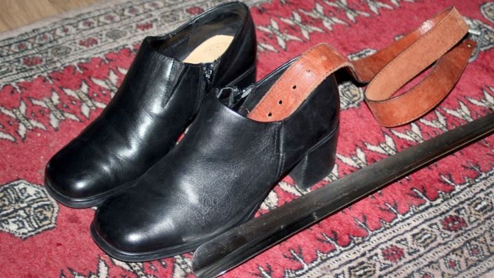 Schwarze Schuhe liegen auf einem Teppich, neben einem Schuhanzieher aus Holz, der zur Erleichterung des Anziehens dient.