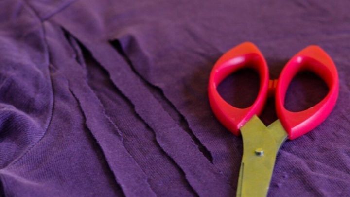 Ein lila T-Shirt liegt auf einem Holztisch, w&auml;hrend eine Schere daneben liegt, bereit f&uuml;r das Schneiden.