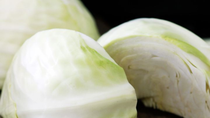 Ein wei&szlig;er Kohlkopf liegt auf einem Holzbrett, gleichm&auml;&szlig;ig d&uuml;nn geschnitten und zeigt frische, saftige Bl&auml;tter.