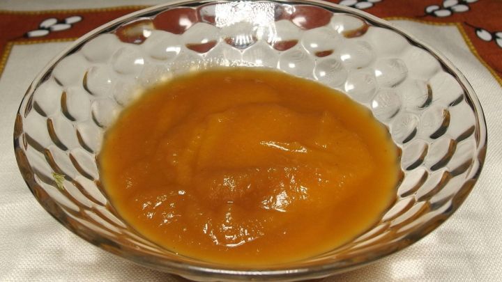 Ein Glas mit Apfelmus steht auf einem Tisch mit hellem Tischdecke, umgeben von einem dekorativen Rand im Hintergrund.