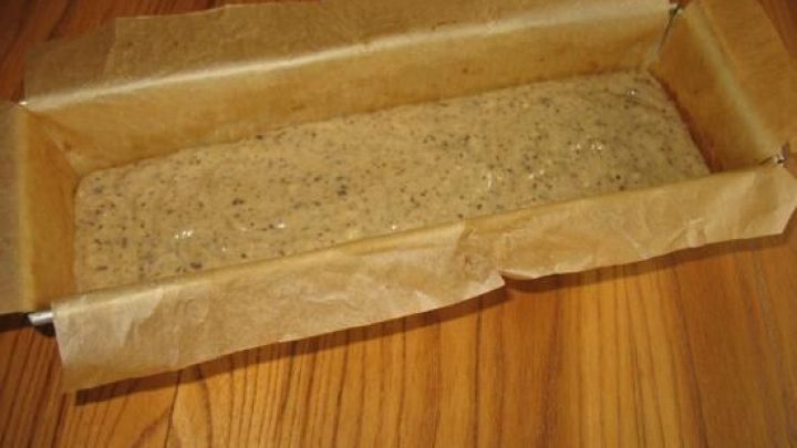 Ein vorbereiteter Kasten mit einem rohen Schoko-Mandel-Kuchen-Teig darauf, platziert auf einem Holztisch.