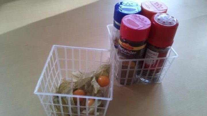 Ein kleiner, wei&szlig;er Korb mit Gew&uuml;rzen steht neben einem anderen Korb, der mit Deko gef&uuml;llt ist. Der Tisch ist hell.