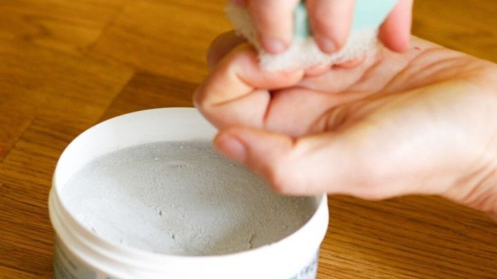 Eine Hand streut ein Pulver aus einer offenen wei&szlig;en Dose auf die andere Handfl&auml;che, um gelbe N&auml;gel durch Nagellack oder Rauchen zu behandeln.