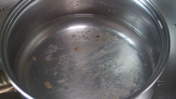 Ein angebranntes Kochgeschirr steht auf einer Sp&uuml;le, mit sichtbaren R&uuml;ckst&auml;nden und Kratzern im Innenbereich.