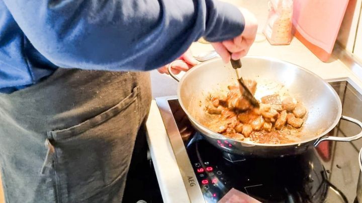 Eine hohe Pfanne wird auf dem Herd genutzt, um Fleischst&uuml;ckchen in einer K&uuml;che zu braten.