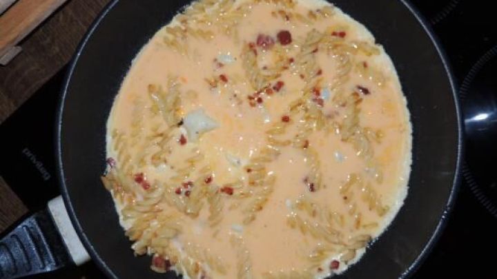 In einer Pfanne wird eine Tortilla zubereitet, w&auml;hrend sie in einer Mischung aus Ei und anderen Zutaten br&auml;t.