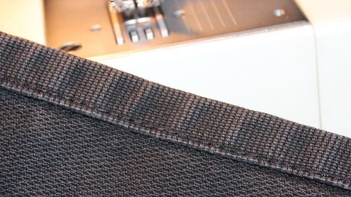 Eine hochwertige N&auml;hmaschine n&auml;ht eine pr&auml;zise Naht auf dunklem Stoff, umgeben von einem hellen N&auml;harbeitsplatz.