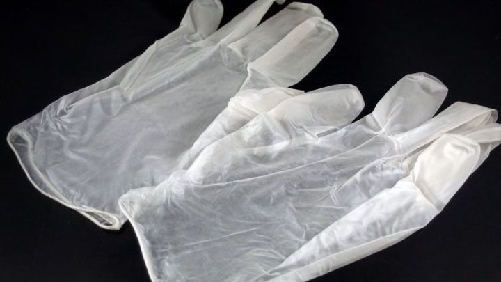 Latex Einweghandschuhe liegen zusammengeklebt auf einem dunklen Untergrund, bereit f&uuml;r den Einsatz.