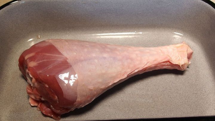 Ein gro&szlig;es H&auml;hnchenschenkel liegt frisch in einer Backform und wartet darauf, zubereitet zu werden.