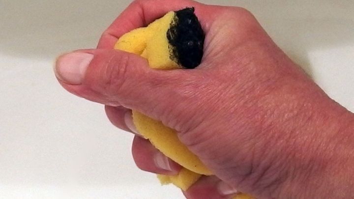 Eine Hand dr&uuml;ckt einen gelben Wischschwamm aus, der &uuml;ber einem Waschbecken gehalten wird.