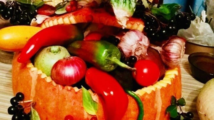 Ein K&uuml;rbis dient als dekorativer Beh&auml;lter, gef&uuml;llt mit frischem Obst und Gem&uuml;se, umgeben von herbstlichen Elementen.