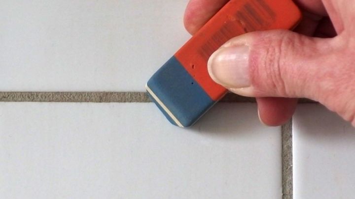 Ein Radiergummi wird verwendet, um die hellen Fliesenfugen zu reinigen, w&auml;hrend eine Hand das Werkzeug sicher f&uuml;hrt.