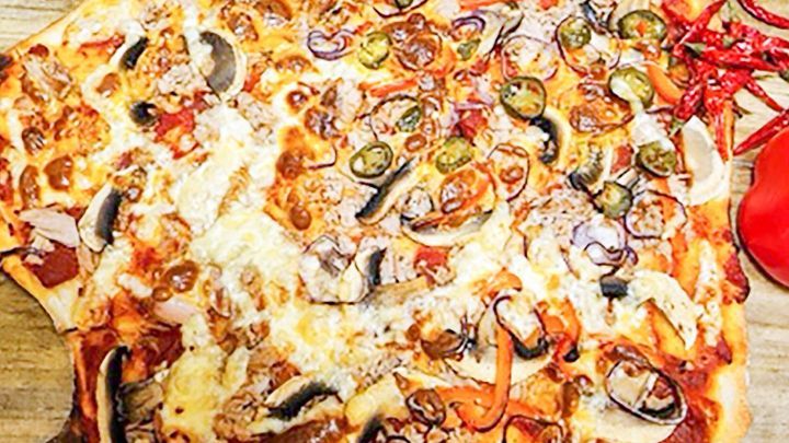 Eine gro&szlig;e Seemannspizza liegt auf einem Holzbrett und ist reich garniert mit verschiedenen Zutaten und Gew&uuml;rzen.