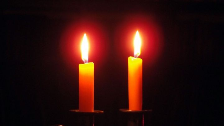 Zwei Spitzkerzen stehen stabil in einem Leuchter, ihre Flammen leuchten in einem dunklen Raum und verbreiten warmth.