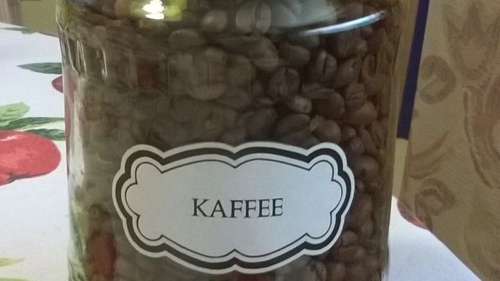 Ein Glas mit Kaffeebohnen steht auf einem Tisch mit Obstmotiv, zur Wiederverwendung von Marmeladengl&auml;sern.