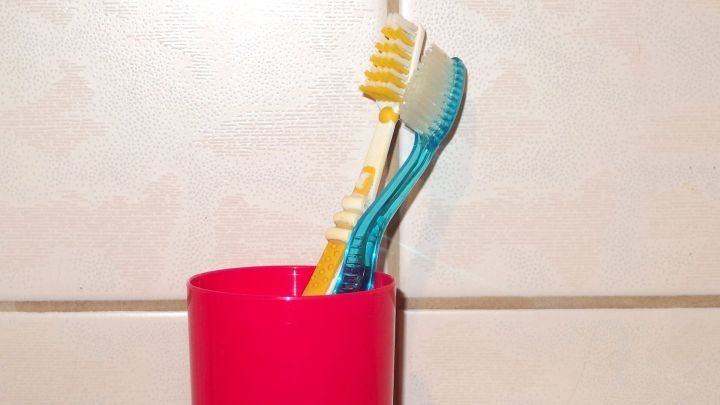 Ein Zahnputzbecher steht auf einer Fliese, zwei Zahnb&uuml;rsten ragen heraus, bereit zum Z&auml;hneputzen und Wasser sparen.